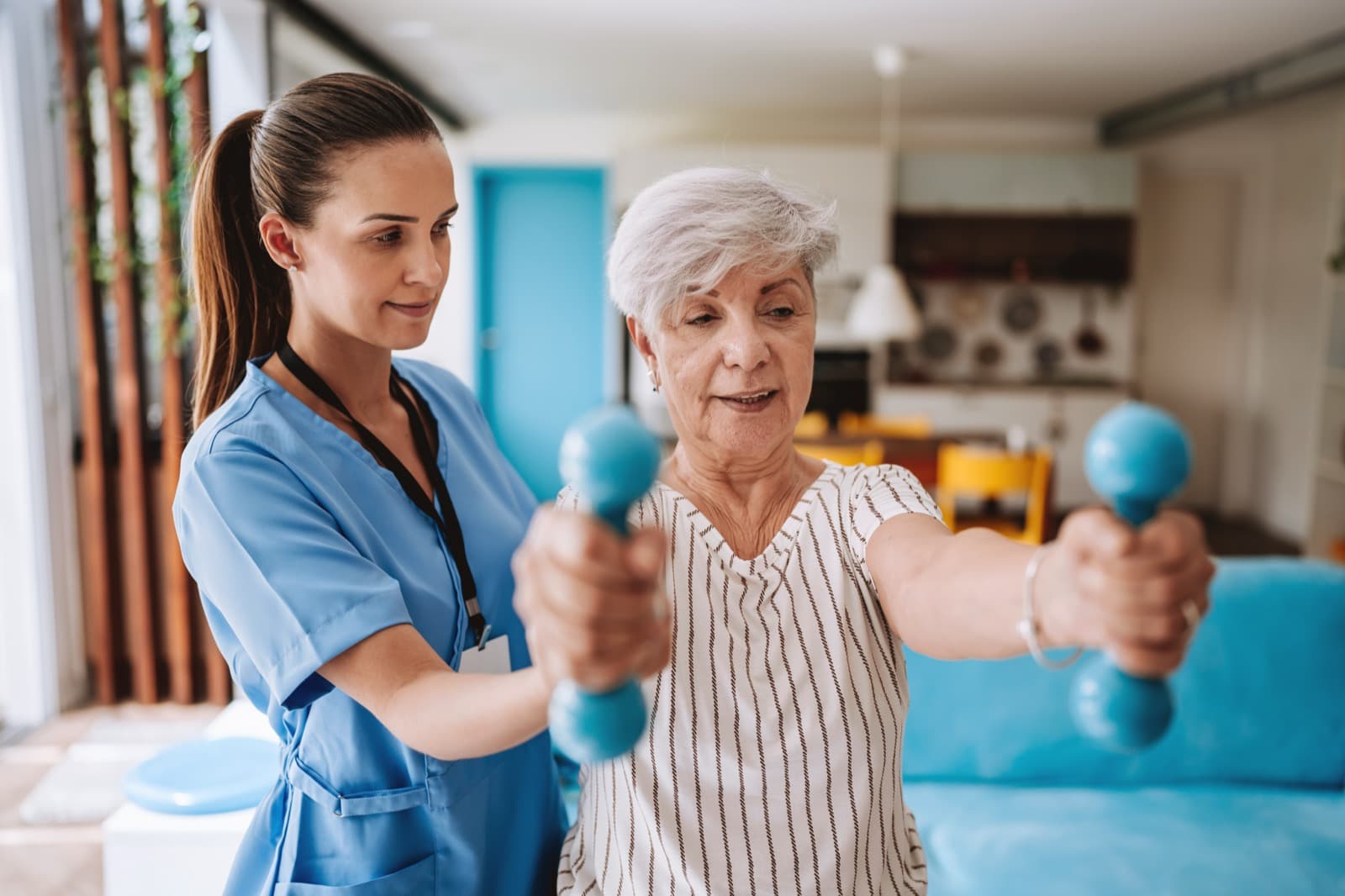 Home physiotherapy session — physiotherapist guiding an elderly patient through a dumbbell exercise