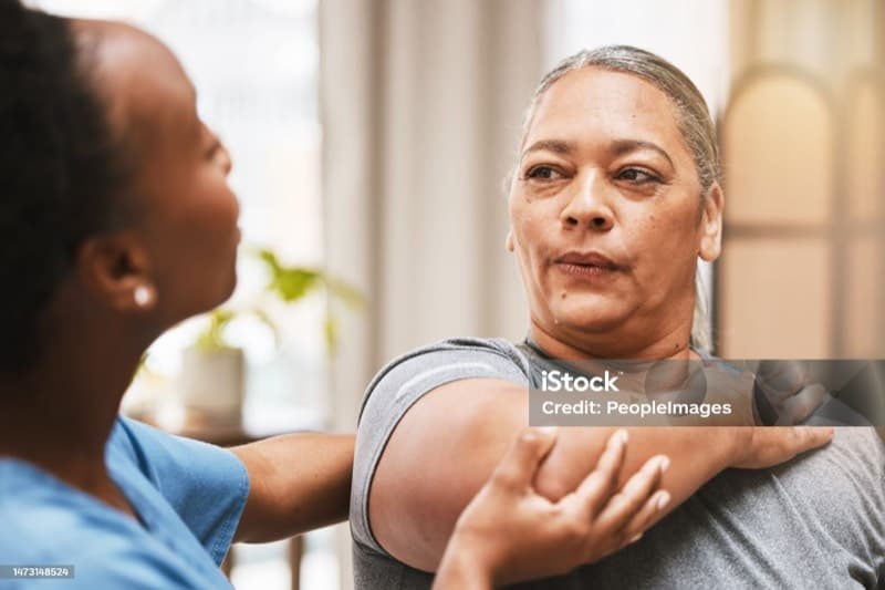 Physiotherapist assessing a patient's shoulder during a private home visit